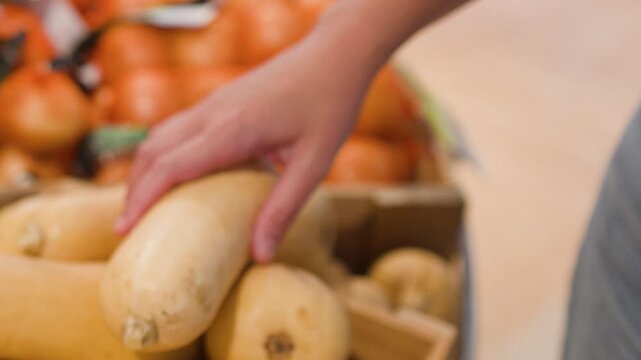 Customer Hand Selecting Organic Butternut Squash in Grocery Store Produce Section