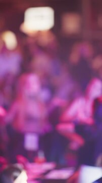 Crowd illuminated under colorful stage lighting. Audience blurred with vibrant purple illumination on stage