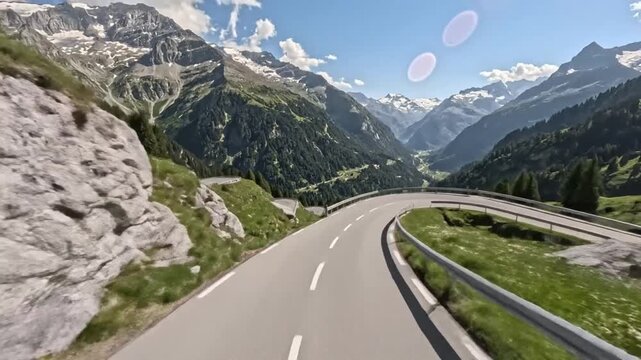 Scenic alpine road curving through lush mountain valley with breathtaking snow-capped peaks and vibrant blue sky