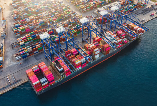 High aerial view of a docked super container cargo ship being unloaded by cranes in a commercial terminal