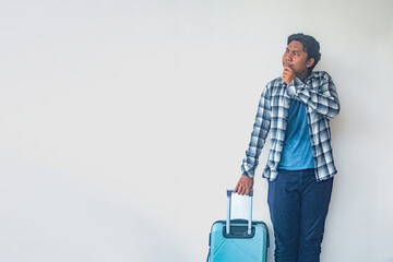 A man in a plaid shirt and blue jeans stands against a plain wall, holding a suitcase and making a surprised or waiting gesture. This image is ideal for travel or waiting themes © Anzz Stock