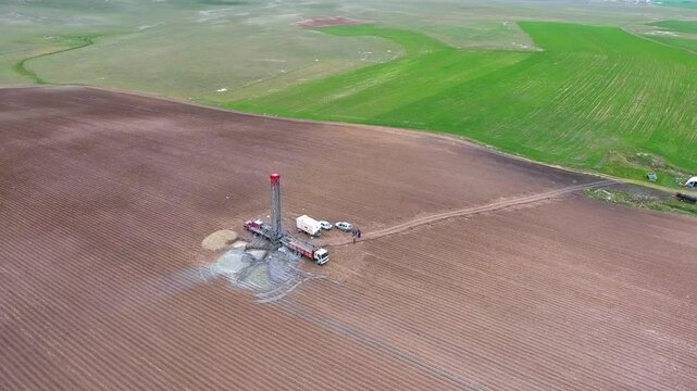 Workers drill a water well in farmland, surrounding the rig with trucks and field equipment. Borehole crew and rural machinery create an industrial agriculture scene with practical purpose.