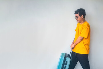 A man in a yellow shirt and black pants is pulling a blue suitcase against a plain background. The image is suitable for themes related to travel, vacation, or airport scenes © Anzz Stock