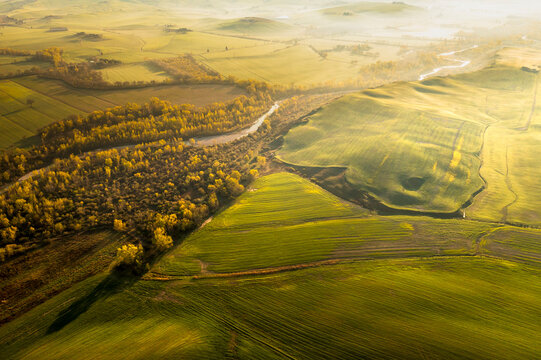 Tuscany aerial landscape showcasing rolling green fields, golden autumn trees, and a winding river in misty morning light, a prime tourism destination in Orcia valley, Pienza, Tuscany, Italy.
