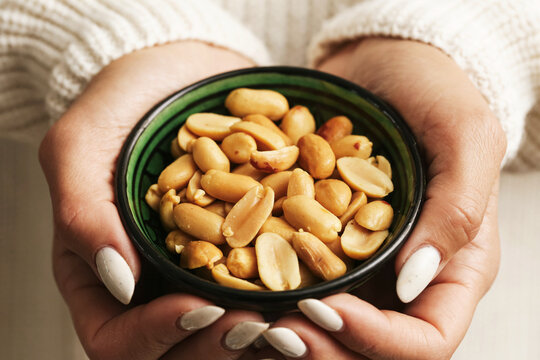 Woman holding bowl with peanuts close up. Healthy roasted nut snack and natural protein source. Organic vegetarian food and everyday nutrition lifestyle indoors at home kitchen table