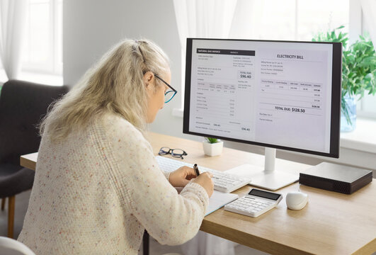 Senior woman checks bills and budget. At home she reads an electricity bill and uses a calculator to track monthly expenses and prepare timely payment. Clear concept of finance management.