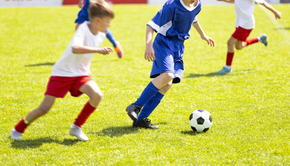 Obraz premium Close-Up of Junior Football Players Competing for Ball on Pitch - Youth Soccer Match Action Between Players in Blue and White Uniforms