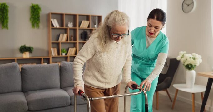 Senior nurse caregiver support walker rehabilitation homecare. Compassionate healthcare professional helps elderly woman with limited mobility during recovery at home. Clear focus on safe care.