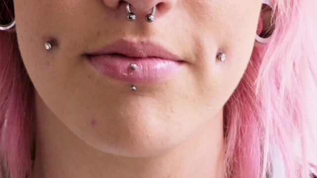 Woman, closeup and smile with piercing in lips, septum and pink hair with earrings for style. Person, mouth and hairstyle with stud in cheeks, facial beauty or confidence with body art on skin
