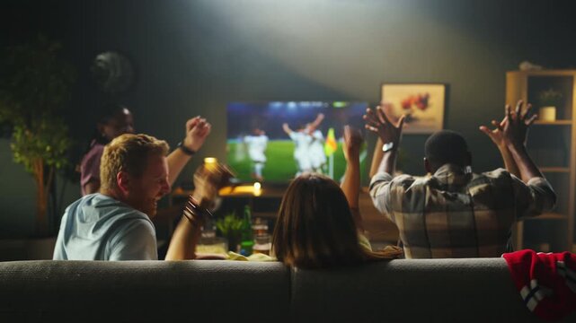 Four friends sit on a couch enjoying a soccer game on TV. They show excitement as they cheer for their teams during the match while eating snacks.