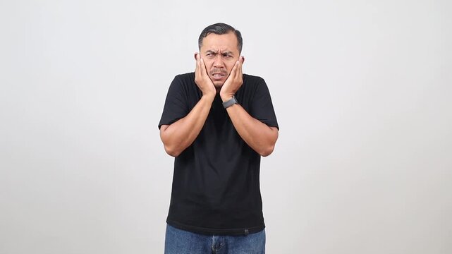 Unhappy Asian man annoyed with loud noise, covering ears with his palms, avoids bad sound, frowns in dissatisfaction