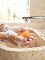 Fototapeta premium Close up of hands washing with natural persimmon soap bar and white foam under running water faucet