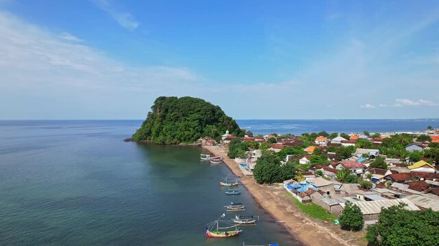 Aerial drone footage of Pecaron village nearby the white sand beach, little peninsula hill with forests,  in Situbondo regency, Java island, Indonesia, quiet sea water bay, colorful wooden fish boats