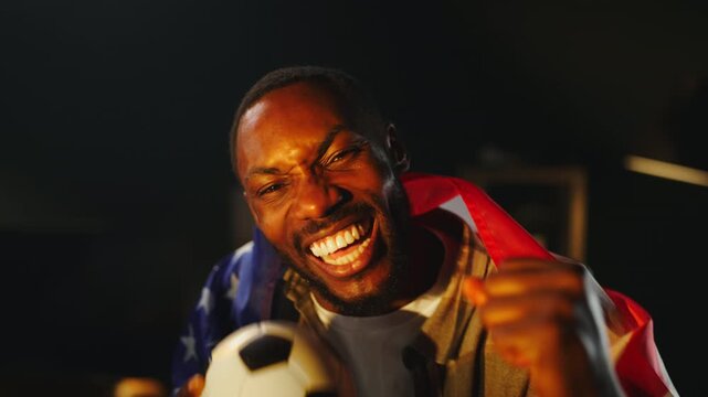 A person wrapped in a flag celebrates soccer with joy. They hold a ball and cheer for the USA team. The scene shows the passion fans have for the sport.