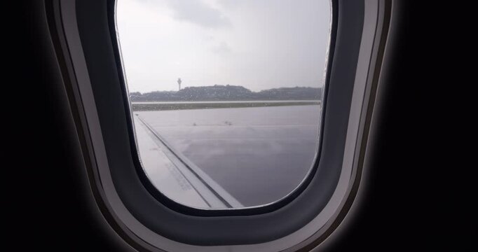 Close-up shot from inside passenger airliner during rainy weather, focusing on water streaks sliding across window as plane accelerates along runway and takes off through light clouds