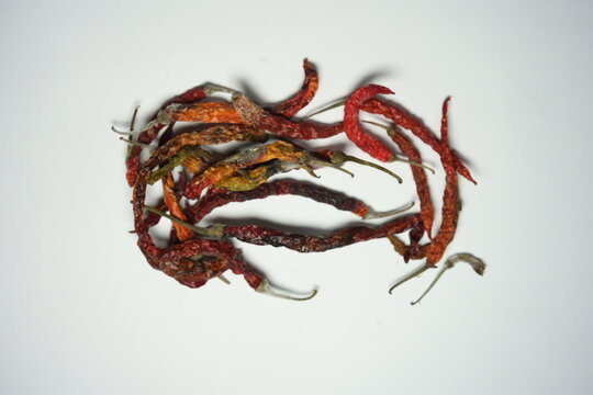 Close up of moldy dried red chili peppers on white background. Rotten dehydrated chilies with visible white fungus and spoilage, isolated top view.