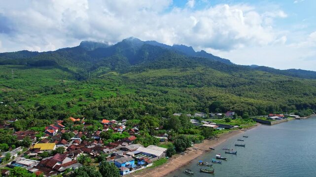 Aerial drone from of Pecaron beach, in Situbondo regency, Java island, Indonesia, white sand, colorful wooden fishing boats, with the local village and Putri Tidur mountain behind with forests, clouds