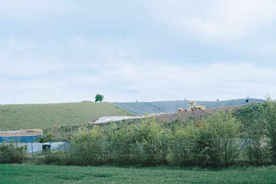 Green grassy hill with industrial landfill and machinery under blue sky, environmental transformation concept, rural landscape, sustainable development.