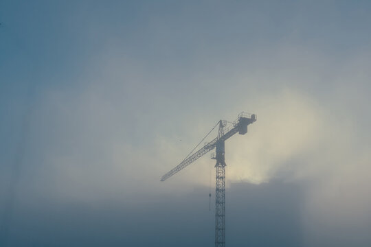 Construction site in the morning fog. Construction cranes above the new buildings in the dense early morning fog.