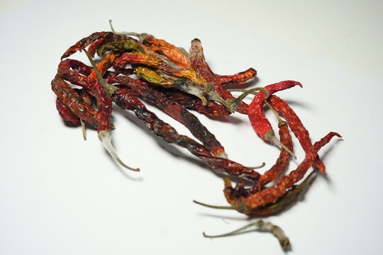 Close up of moldy dried red chili peppers on white background. Rotten dehydrated chilies with visible white fungus and spoilage, isolated top view.