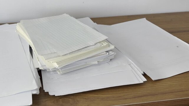 Video of scattered papers spread across a desk. Messy workspace scene representing stress, paperwork, office chaos, disorganization and busy work routine.
