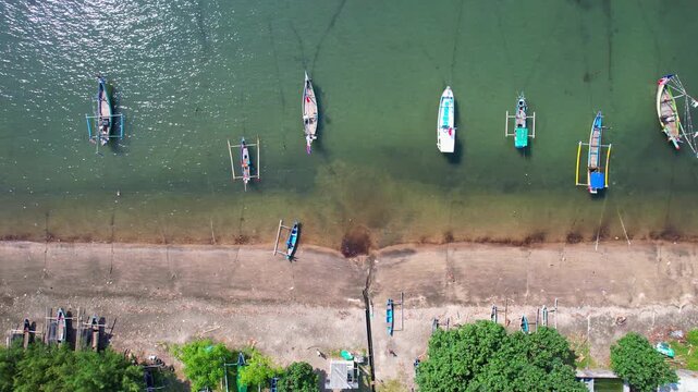 Aerial drone from above of Pecaron beach, in Situbondo regency, Java island, Indonesia, with white sand, colorful wooden fishing boats at anchor, turquoise and green water, sunny weather