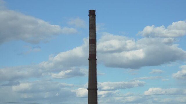 Single inactive industrial smokestack against dramatic blue sky with clouds. Handheld 4K footage of abandoned industrial infrastructure and post industrial landscape.