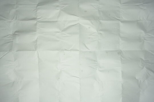 Texture of crumpled and folded white paper. Background of messy creased paper sheet with grid lines from folding, top view surface texture.