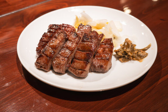 Thick cut grilled beef tongue served with pickled cabbage on white plate