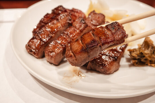 Thick cut grilled beef tongue served with pickled cabbage on white plate