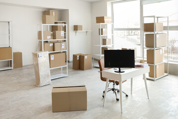 Fototapeta premium Interior of light warehouse with workplace, shelf units and cardboard boxes