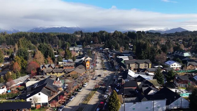 Avenida Arrayanes in Villa La Angostura Los Lagos Department Neuqu&eacute;n Patagonia Argentina showing central corridor with alpine architecture, vehicles, dense forest and snowy Andes ridge lateral slide