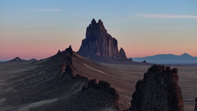 Drone tracks steadily along a jagged ridge, maintaining low altitude with Shiprock rising beyond the sunrise desert expanse