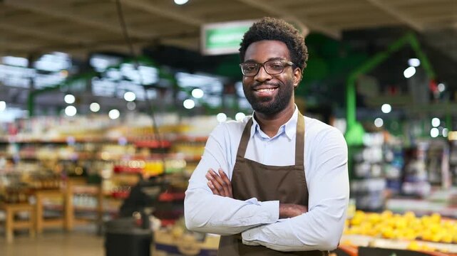 Portrait of smiling african american salesman standing in grocery store looking at camera. Successful greengrocer small business owner in market. Headshot of happy black man worker in apron. Close up