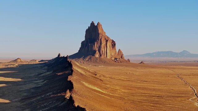 Expansive drone shot captures Shiprock surrounded by endless desert plains, distant mountains, and open sky