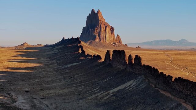 Drone slowly rises from low altitude, revealing Shiprock emerging above the desert horizon and surrounding terrain