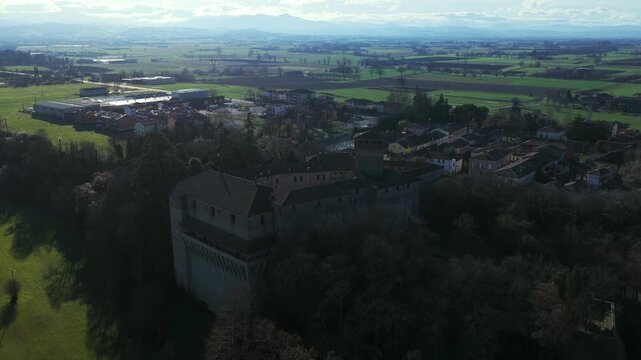 Aerial push-in over Montechiarugolo Castle, revealing the medieval fortress and village surrounded by open countryside in Emilia-Romagna, Italy