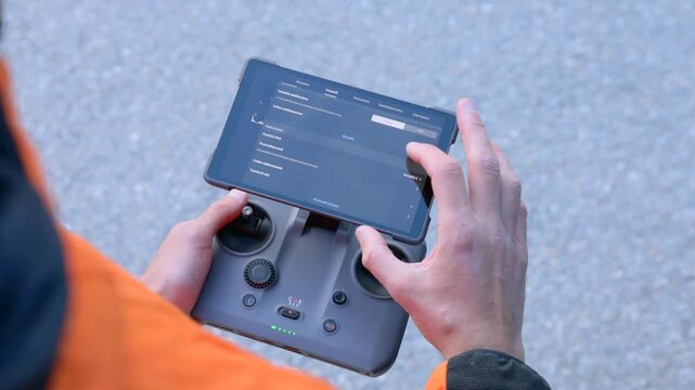 Hands adjust settings on a tablet-mounted drone controller before flight. Pre-flight configuration and safety checks for aerial filming