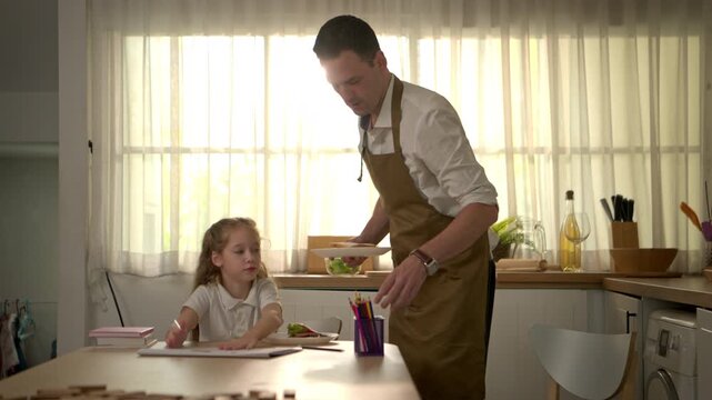 The father lovingly prepared dinner, watching over his daughter as she did her homework in the kitchen, in a warm, family atmosphere