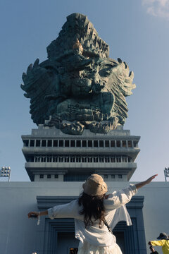 Female tourist in hat posing in front of the Garuda Wisnu Kencana statue in Bali, Indonesia, famous cultural landmark and travel destination.