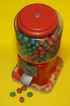 A vintage candy dispenser filled with colorful candies on yellow background