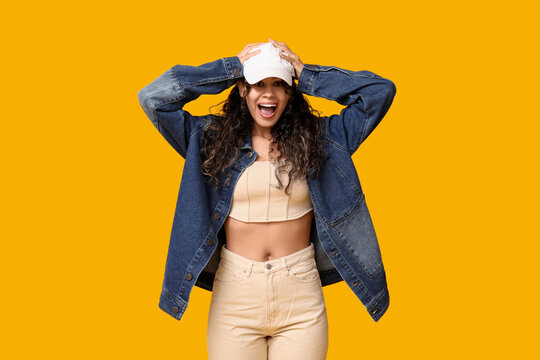 Happy African-American woman in baseball cap and stylish clothes on yellow background
