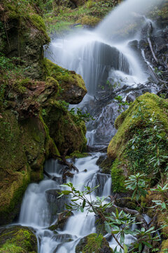 The Veins of the Mountain. A stunning vertical composition of a cascading waterfall rushing over moss-laden rocks, capturing the raw power and movement of nature in a single frozen moment 