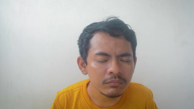 Man with dark hair and mustache wearing a yellow shirt looking forward with a neutral expression and messy hair
