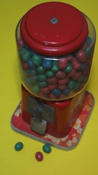 A retro gumball machine with colorful candy on yellow background ready to dispense by a hand.