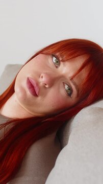 Young woman at home feels so exhausted and in bad mood after tough news stares at screen sighs softly. Redhead girl on sofa lowers gaze slow breath low energy no drive needs rest and calm before tasks