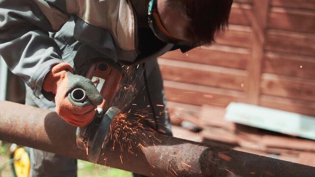 Close up of industrial technician using electric grinder on rusty steel pipe at construction site. Bright sparks illuminate professional manual work, engineering process and heavy production industry.