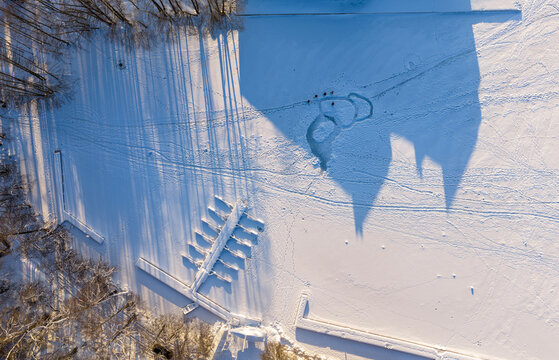 Aerial view of the long shadows of Trakai Island Castle cast over the snow-covered frozen Lake Galve with a wooden pier and winter trees in Trakai, Vilnius County, Lithuania.