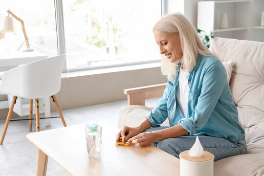 Mature woman taking pills from daily pillbox at home