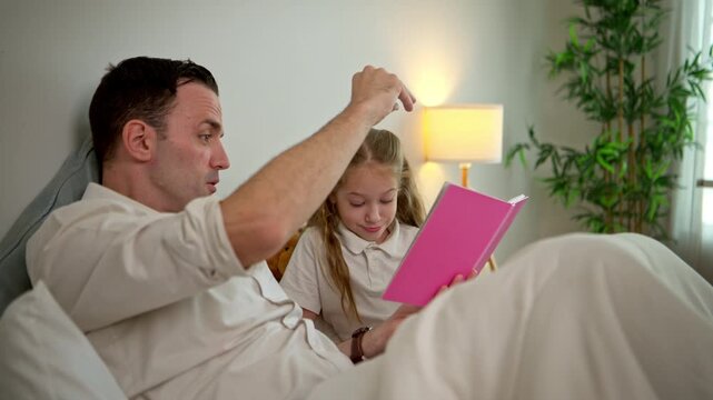Father  reading a bedtime story together to daughter on the bed with funny facial expressions in a cozy bedroom